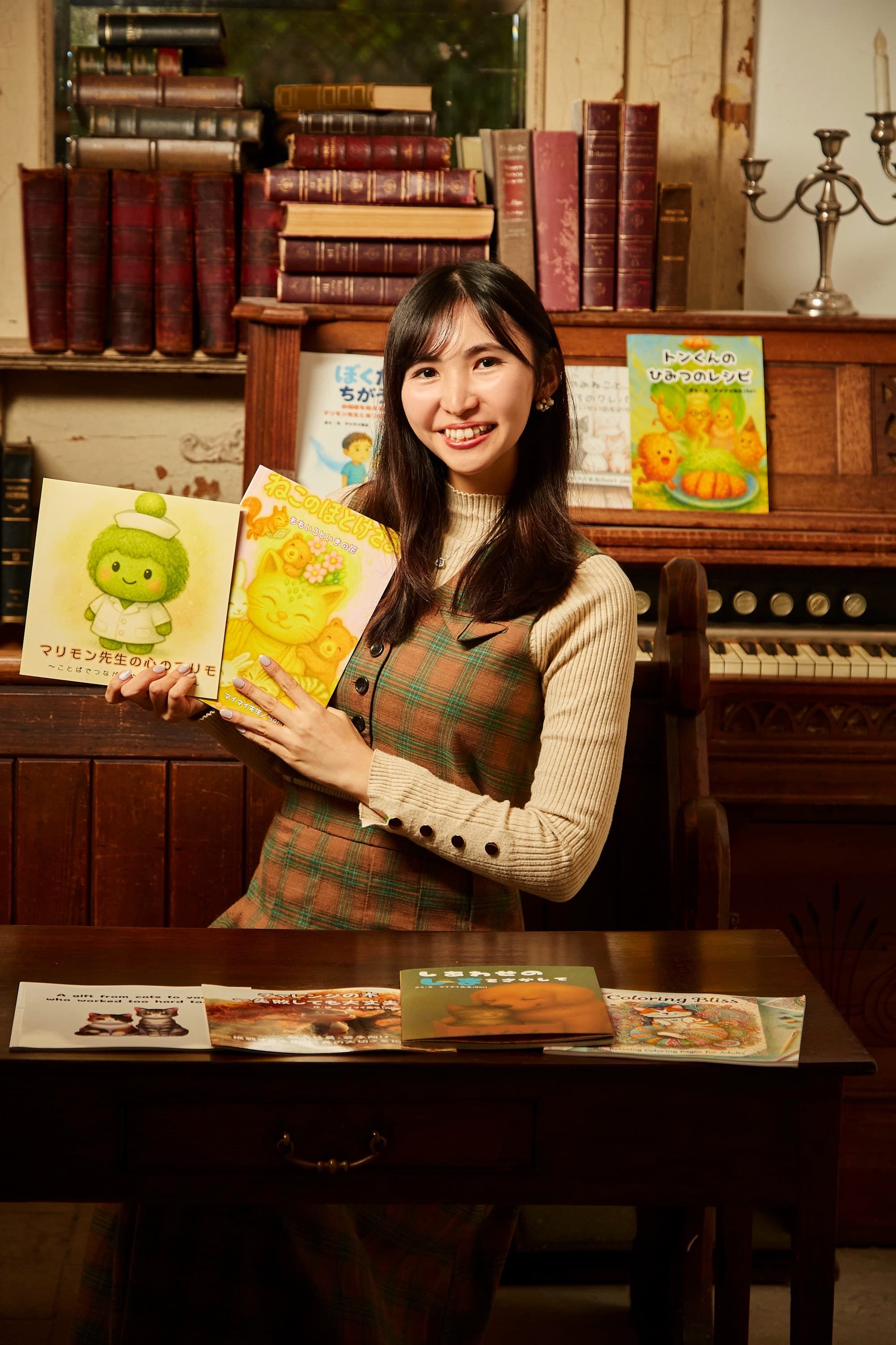 絵本を手にする maimai と、これまでに描いた絵本たち